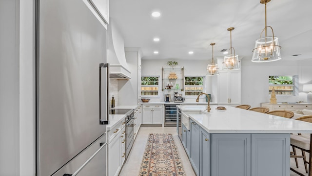 kitchen featuring hanging light fixtures, a kitchen bar, an island with sink, beverage cooler, and high quality appliances