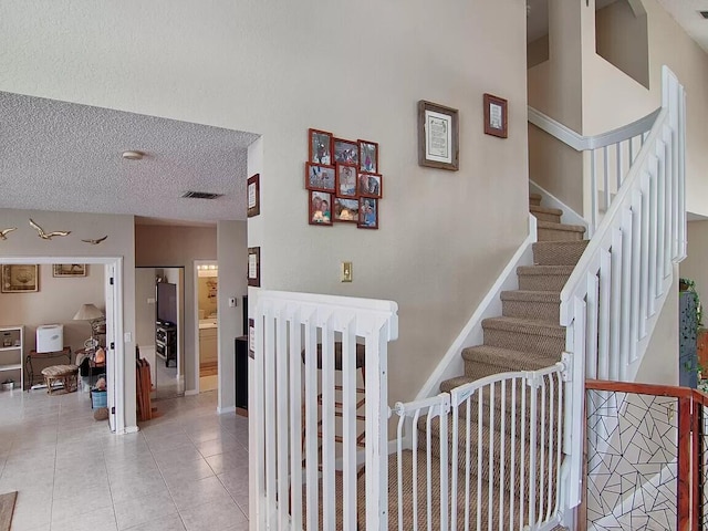 stairway featuring a textured ceiling, light tile floors, and a high ceiling