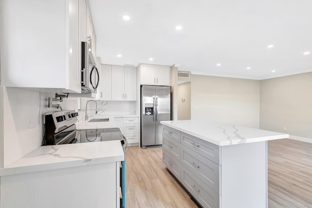 kitchen featuring stainless steel appliances, tasteful backsplash, white cabinetry, light wood-type flooring, and light stone counters