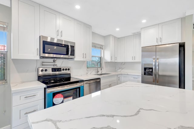 kitchen with light stone countertops, white cabinetry, sink, and stainless steel appliances