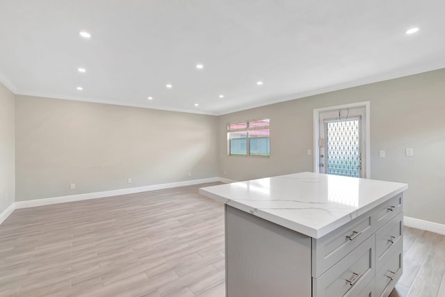 kitchen with gray cabinets, crown molding, a kitchen island, light stone countertops, and light wood-type flooring