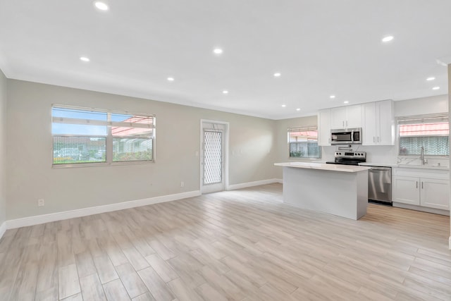 kitchen with light wood-type flooring, a center island, appliances with stainless steel finishes, and white cabinetry