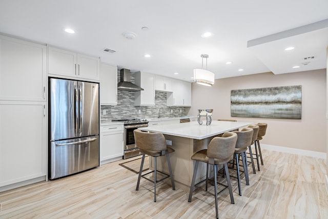 kitchen with white cabinetry, wall chimney exhaust hood, hanging light fixtures, and appliances with stainless steel finishes