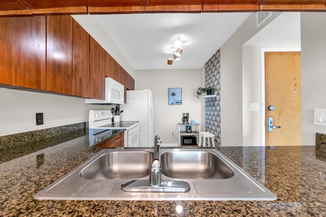 kitchen with dark stone counters, track lighting, white appliances, and sink