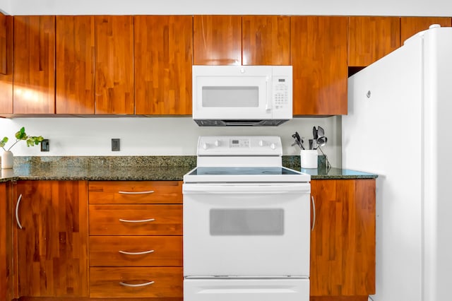 kitchen featuring dark stone counters and white appliances