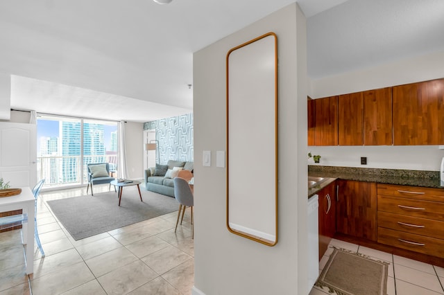 kitchen with light tile floors, dark stone counters, floor to ceiling windows, and dishwasher