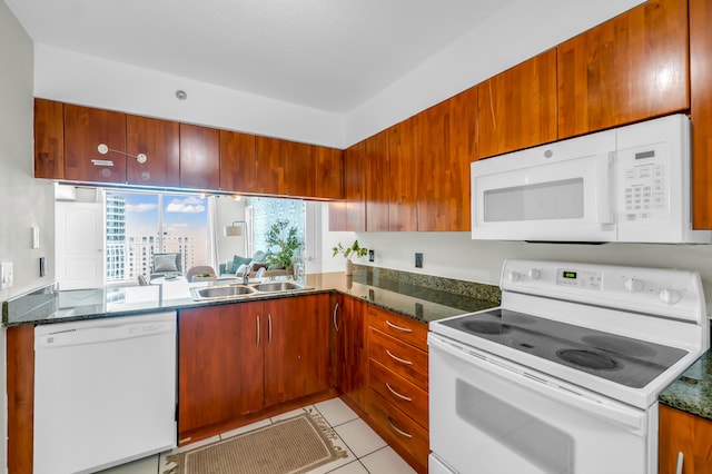 kitchen with white appliances, dark stone countertops, light tile floors, and sink