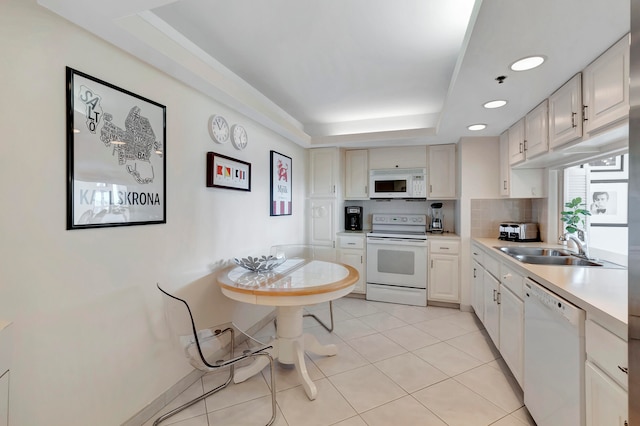 kitchen with white appliances, tasteful backsplash, a tray ceiling, and light tile floors