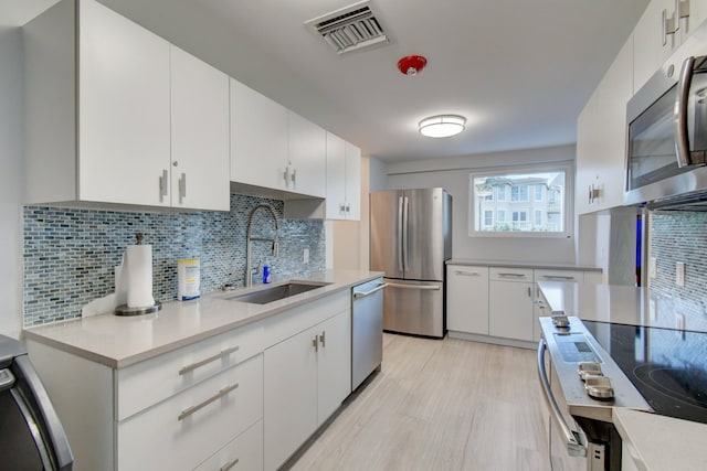 kitchen with stainless steel appliances, white cabinets, backsplash, light wood-type flooring, and sink