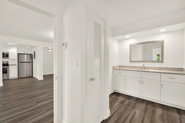 interior space with dark hardwood / wood-style floors, sink, light stone counters, stainless steel appliances, and white cabinetry