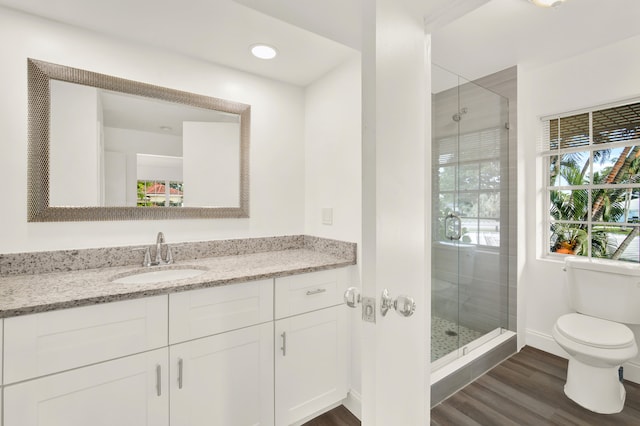 bathroom featuring hardwood / wood-style flooring, walk in shower, vanity with extensive cabinet space, and toilet