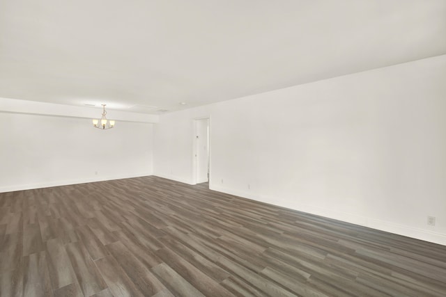 empty room featuring a notable chandelier and dark wood-type flooring