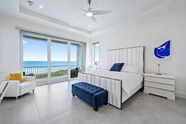 bedroom featuring access to outside, a water view, a tray ceiling, and recessed lighting