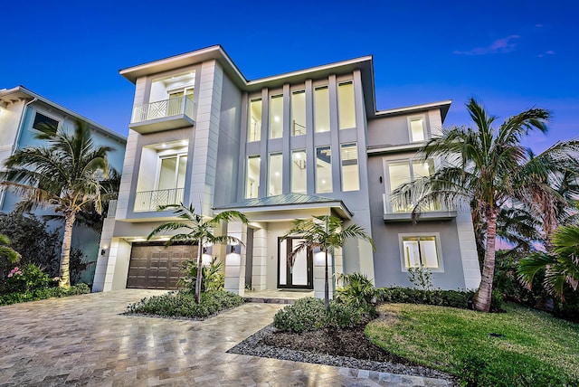 view of front facade featuring a garage, decorative driveway, a balcony, and stucco siding