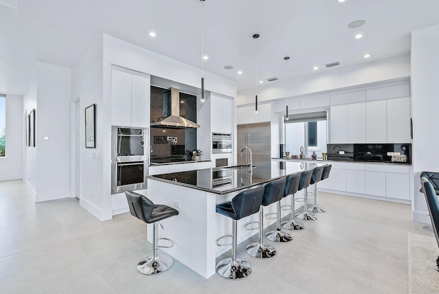 kitchen with dark countertops, decorative backsplash, wall chimney range hood, modern cabinets, and a kitchen breakfast bar