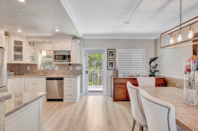 kitchen featuring ornamental molding, appliances with stainless steel finishes, light stone counters, and pendant lighting