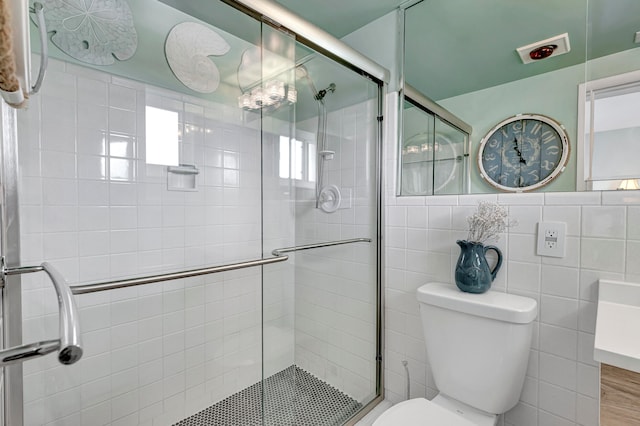 bathroom with tile walls, toilet, a shower with shower door, wood-type flooring, and an inviting chandelier