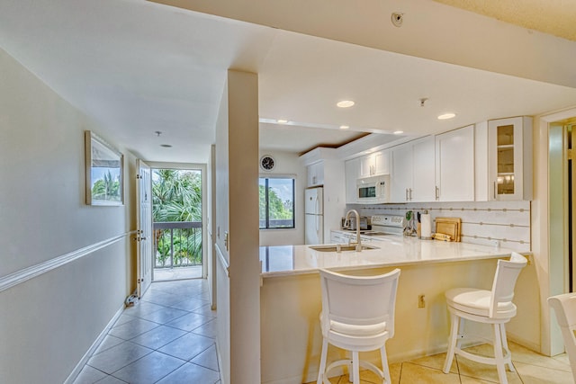 kitchen featuring light tile floors, white appliances, backsplash, white cabinetry, and kitchen peninsula