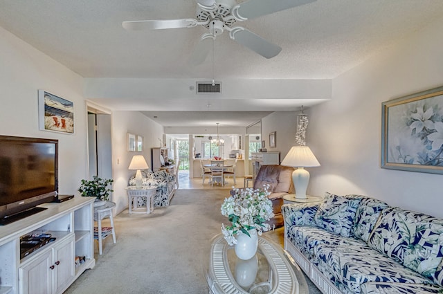 carpeted living room with ceiling fan with notable chandelier and a textured ceiling