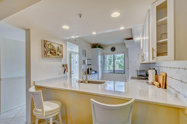 kitchen featuring sink, tasteful backsplash, light tile flooring, kitchen peninsula, and light stone countertops