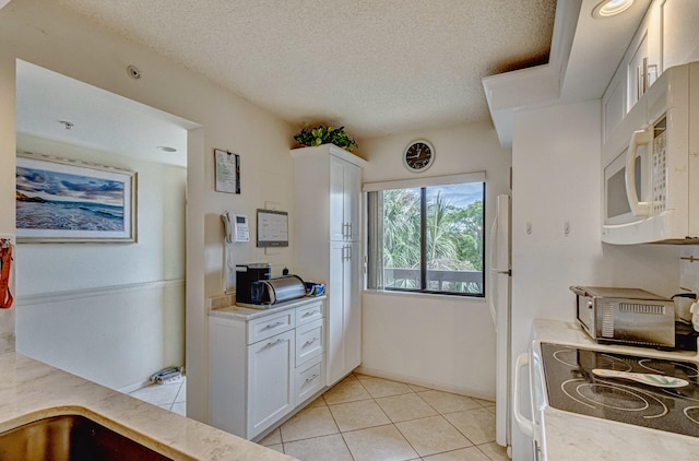 kitchen with a textured ceiling, white cabinetry, light tile floors, and range