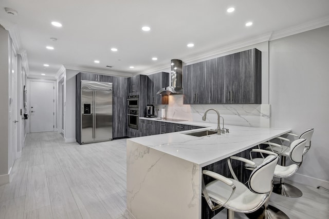 kitchen with sink, kitchen peninsula, wall chimney exhaust hood, stainless steel appliances, and a kitchen breakfast bar