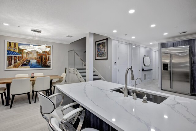 kitchen with light stone counters, light hardwood / wood-style flooring, ornamental molding, sink, and stainless steel built in fridge