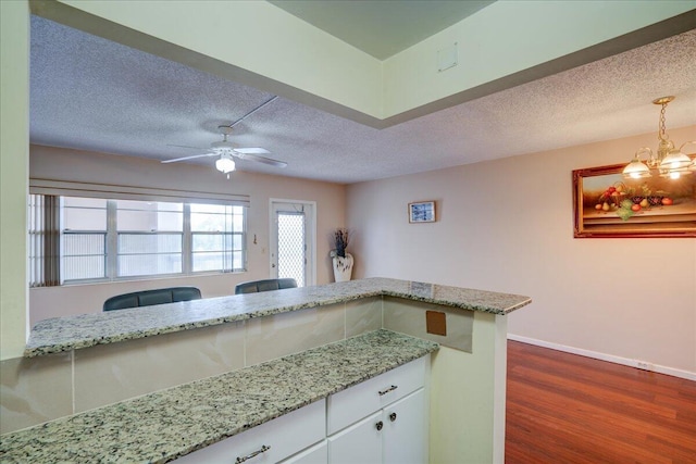 kitchen with ceiling fan with notable chandelier, a textured ceiling, white cabinetry, light stone countertops, and dark hardwood / wood-style floors