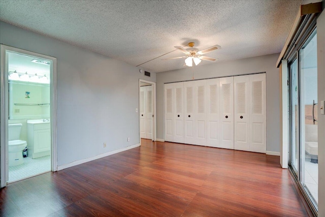 unfurnished bedroom featuring a textured ceiling, wood-type flooring, ceiling fan, multiple closets, and ensuite bathroom