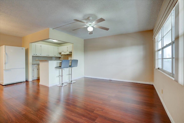 unfurnished living room with dark wood-type flooring, a textured ceiling, and ceiling fan