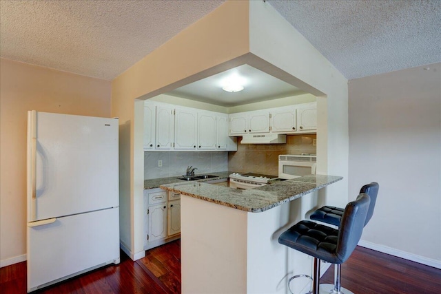 kitchen with white appliances, backsplash, dark hardwood / wood-style flooring, kitchen peninsula, and white cabinets