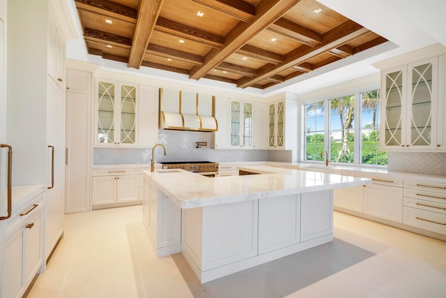 kitchen featuring coffered ceiling, backsplash, light tile flooring, and an island with sink