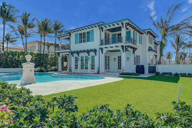 back of property with a balcony, a fenced in pool, a lawn, and a patio