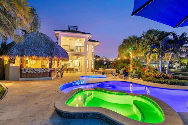 pool at dusk with a patio area, exterior bar, and an in ground hot tub