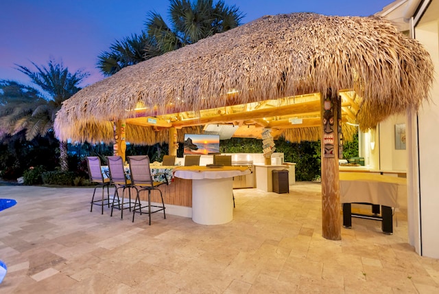 patio terrace at dusk featuring exterior kitchen and an outdoor bar