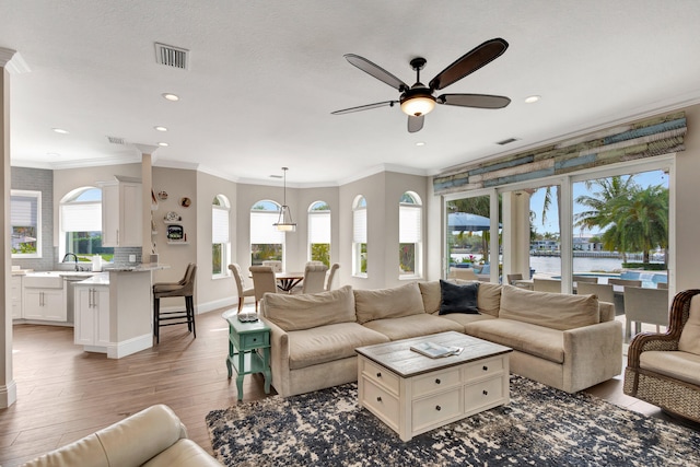 living room with sink, hardwood / wood-style floors, ceiling fan, ornamental molding, and a water view