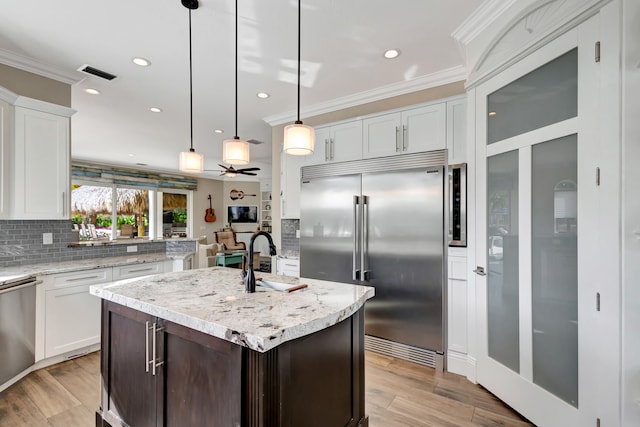 kitchen featuring decorative light fixtures, stainless steel appliances, an island with sink, and white cabinetry