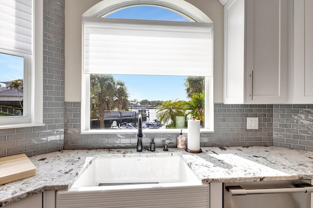 kitchen featuring sink, white cabinets, tasteful backsplash, stainless steel dishwasher, and light stone countertops