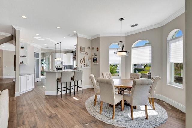 dining space with a healthy amount of sunlight, crown molding, and light hardwood / wood-style flooring