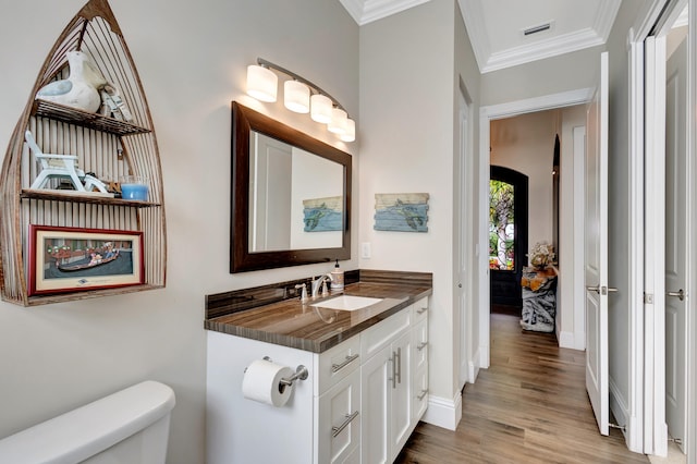 bathroom featuring hardwood / wood-style flooring, crown molding, vanity, and toilet