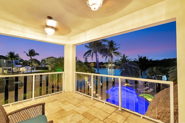 balcony at dusk featuring ceiling fan, a water view, and an in ground hot tub