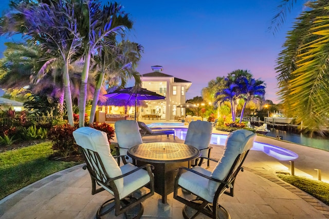 patio terrace at dusk featuring a swimming pool with hot tub