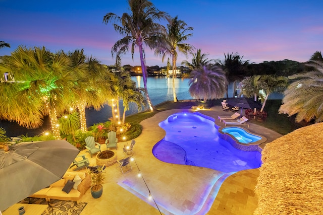 pool at dusk with a fire pit, a patio area, a grill, an in ground hot tub, and a water view