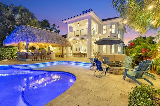 pool at dusk with a bar, an outdoor fire pit, a patio, and ceiling fan