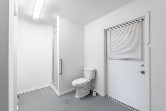 bathroom with toilet, a shower with door, and concrete flooring