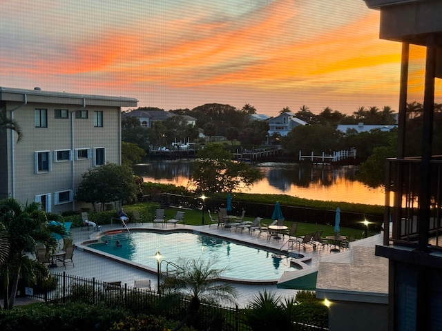 pool at dusk with a patio area and a water view