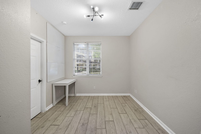 spare room with an inviting chandelier, a textured ceiling, and light hardwood / wood-style floors