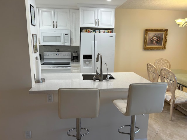 kitchen with white appliances, sink, light tile floors, a kitchen breakfast bar, and white cabinetry