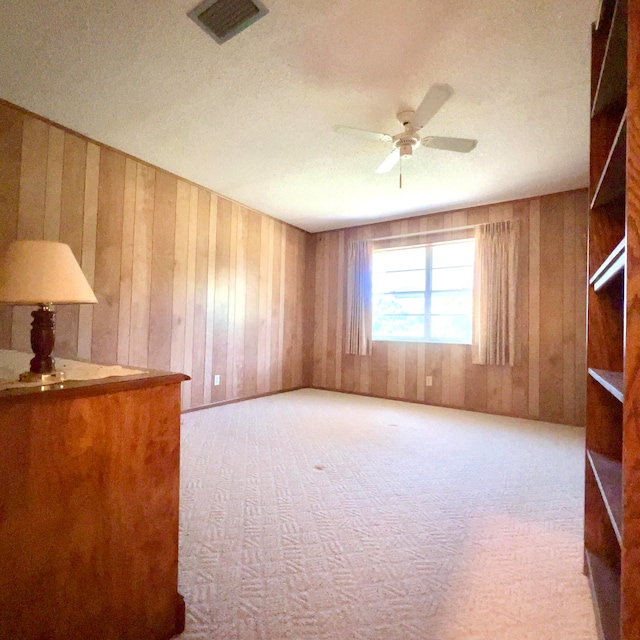 unfurnished room with light carpet, wooden walls, ceiling fan, and a textured ceiling