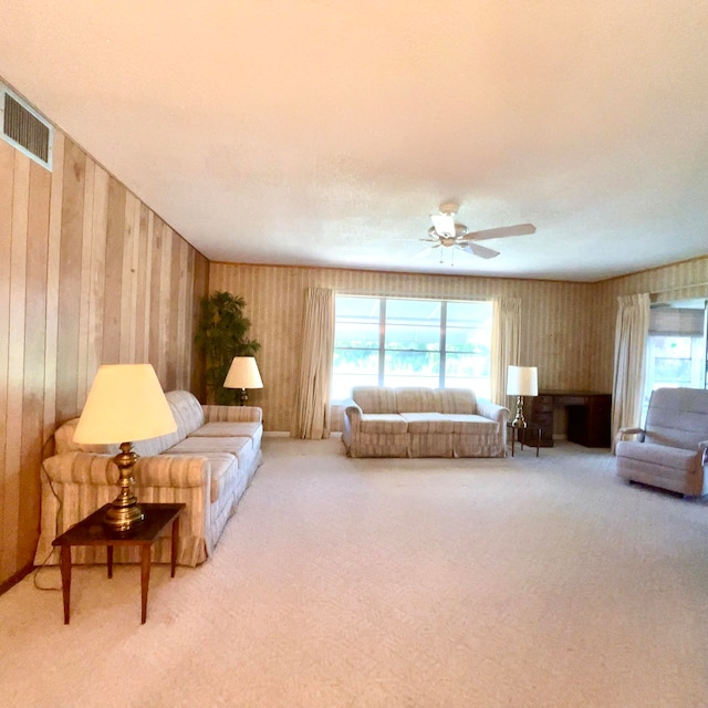 living room featuring ceiling fan, wooden walls, and light colored carpet